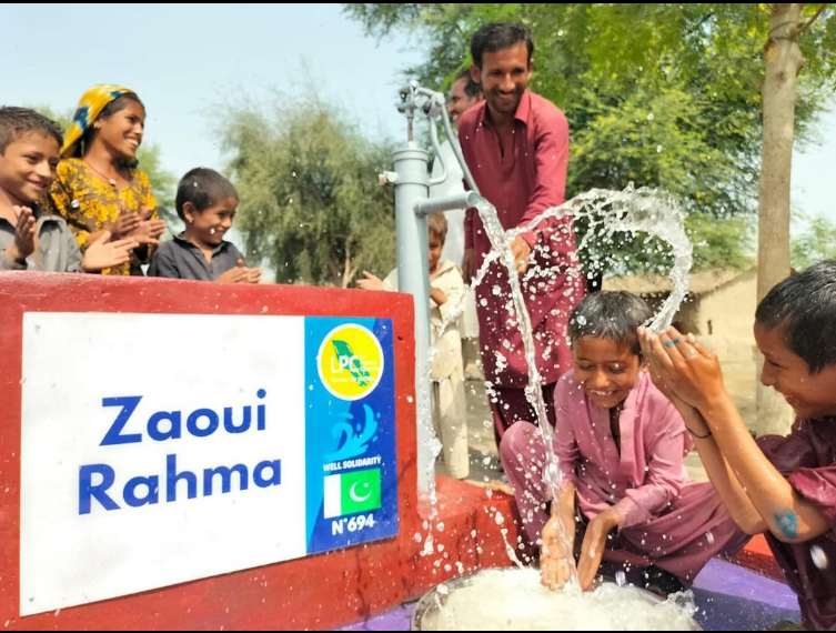 Children laughing around a working water pump.