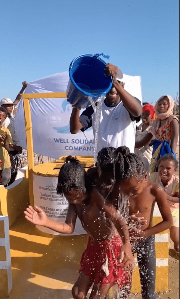 Children playing under water from a bucket.